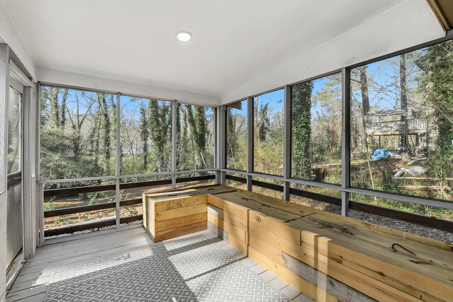 Screened porch with built-in wood bench seating and views of the wooded backyard